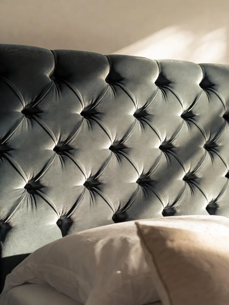 A luxurious gray tufted headboard behind a bed with plush white bedding and decorative pillows, adding elegance and cozine...