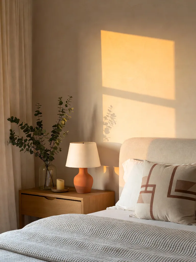 Serene bedroom with a neutral color palette, featuring a light beige bed, soft white bedding, and wood accents.