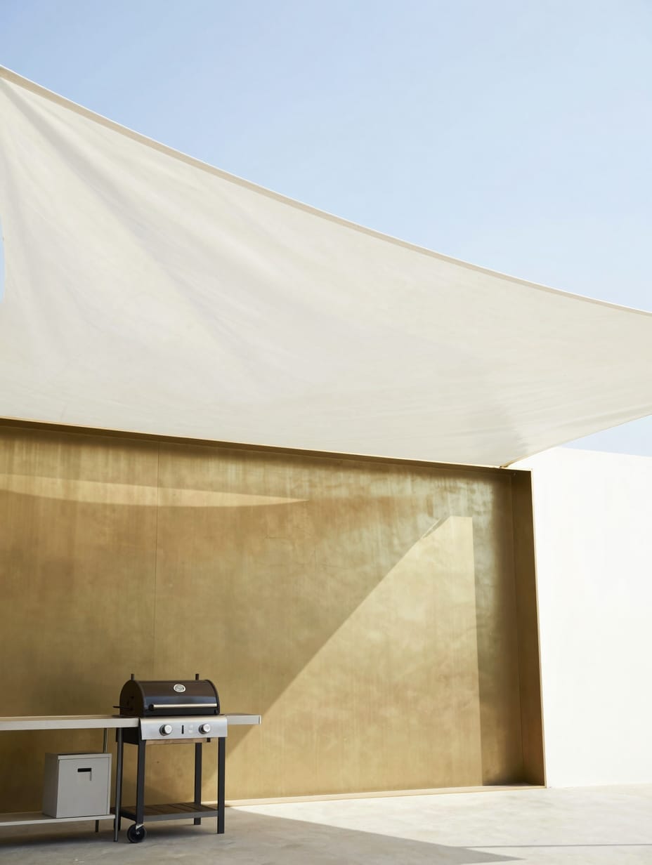 A large tan fabric shade sail stretched over an outdoor kitchen and dining area.